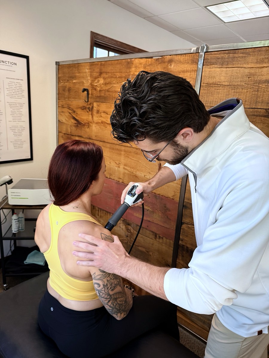 Dr. Coltin Golden treating the back of a patient's shoulder with shockwave therapy at Life Chiropractic in Missoula